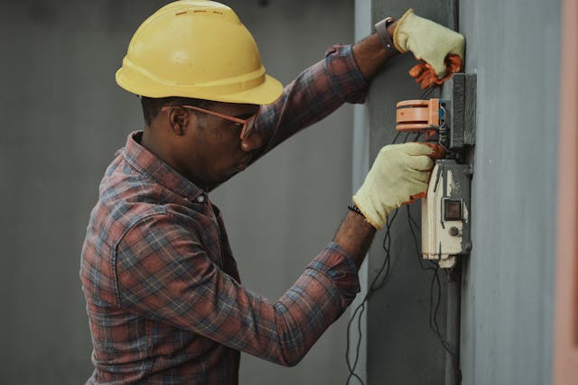 A person wearing a hard hat and gloves while fixing wiring