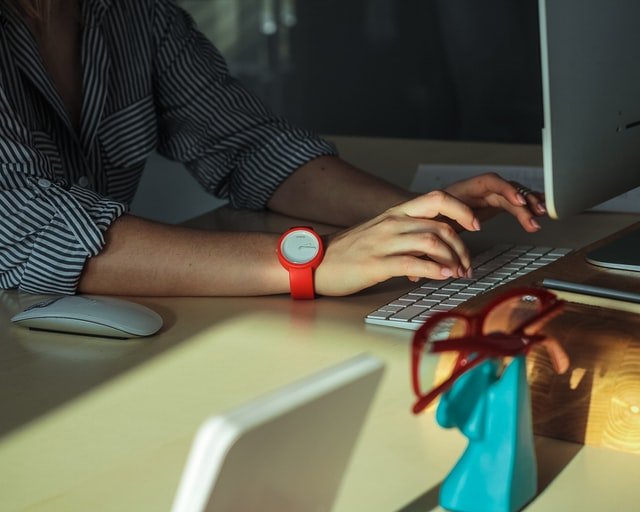 a person wearing a red watch typing on a computer