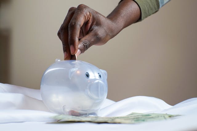 hand putting coins into a clear piggy bank